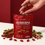 A hand holding ruby softgels above an open Alora pouch with barberry roots and Ceylon cinnamon